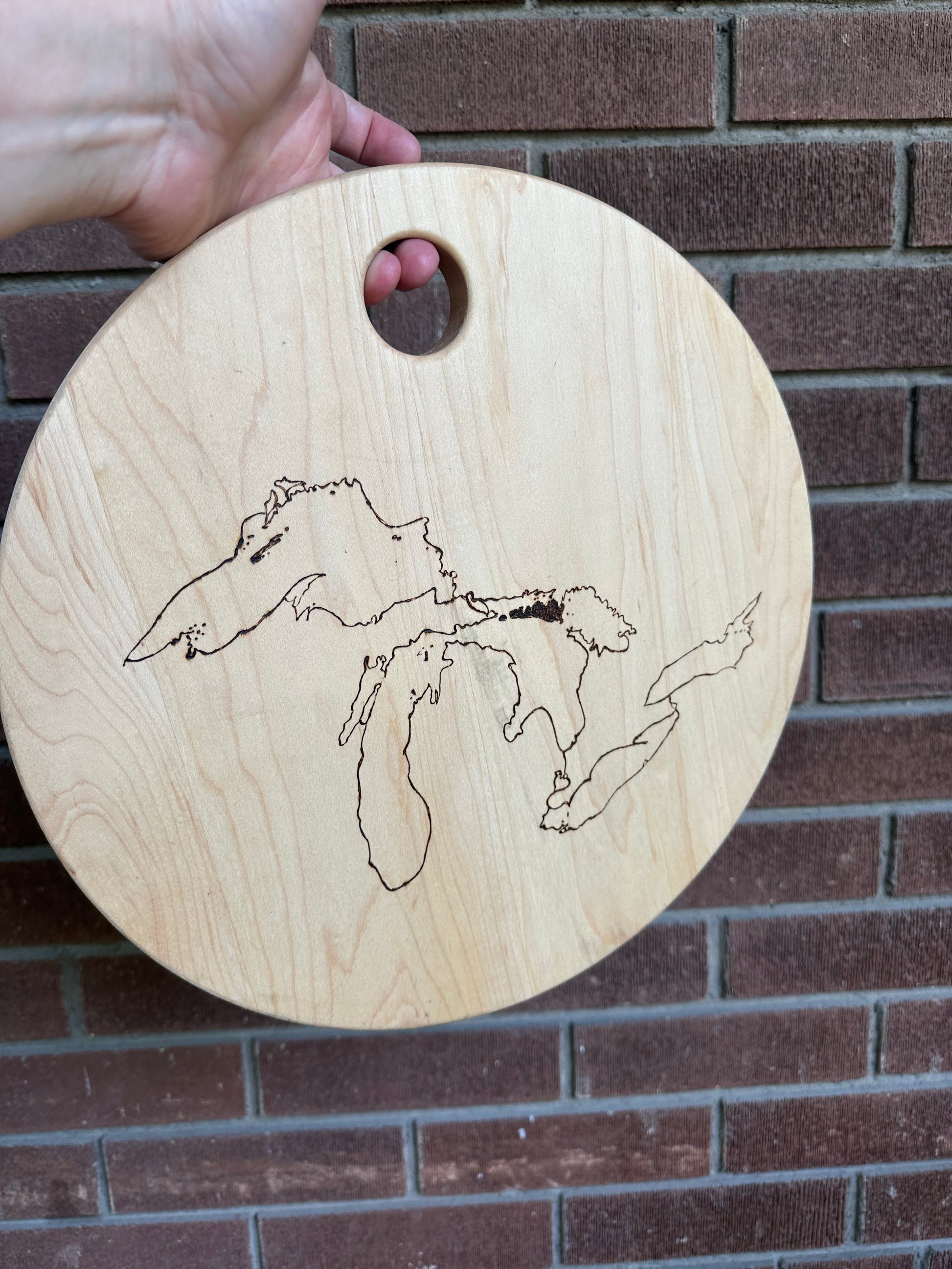Image displays a brick wall in the background with a 13" round serving dish in front. Wood dish has The Great Lakes burned into it using a pyrography machine.